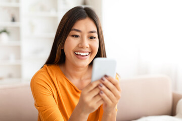 Closeup of smiling young asian woman using smartphone at home,