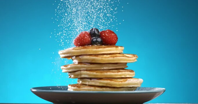 Super slow motion close up of sweet icing sugar powder are falling on sweet delicious dessert american pancakes with honey or caramel syrup and berries isolated on soft colorful background at 1000 fps