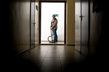 A man is vacuuming in a long hallway. The cleaner is at work.