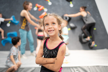 Smiling little girl climber standing arms crossed in sports center. Female child looking up during...