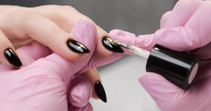 Applying black gel nail polish, close-up. Applying nail polish by nail master in a salon.