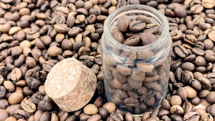 Coffee beans in a small glass jar with a cork lid on the table. Coffee beans packed in a transparent, airtight storage container. Coffee seeds inside a glass jar.