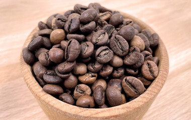 Coffee beans in a wooden plate on the table, top view. A drink made from roasted and ground beans of the coffee tree or coffee bush.