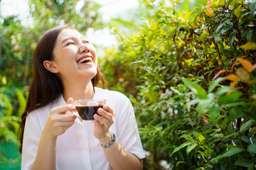 Asian beautiful woman enjoy drinking a cup of coffee in morning at home backyard. Smiling cheerful woman drinks a black coffee in the nature close up.