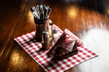 Fototapeta na wymiar Salt, pepper, napkins and cutlery on a wooden table in a pub or restaurant