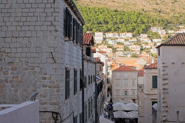 A lively street snakes through the dense, historic limestone buildings of Dubrovnik, with hillside old homes in the background