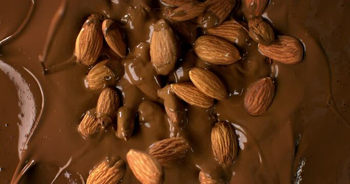 Super slow motion macro of bio organic almond nuts falling in creamy melted liquid dark cocoa chocolate with splashing dripping drops at 1000 fps.