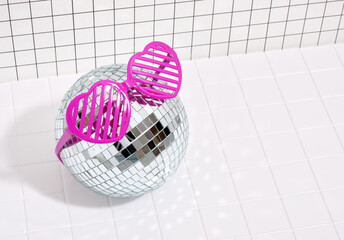 Trendy pink heart shaped glasses lie on a mirrored disco ball. Fashion look and disco. Copy space for text.
