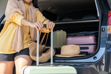 A young woman is preparing to load her travel bag at the back of the car in preparation for a...