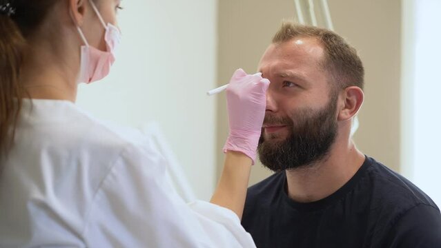 The cosmetologist marks with a pencil the points for beauty injections of botulinum therapy on the face of a man. Concept Plastic surgery and cosmetology for men with copy space