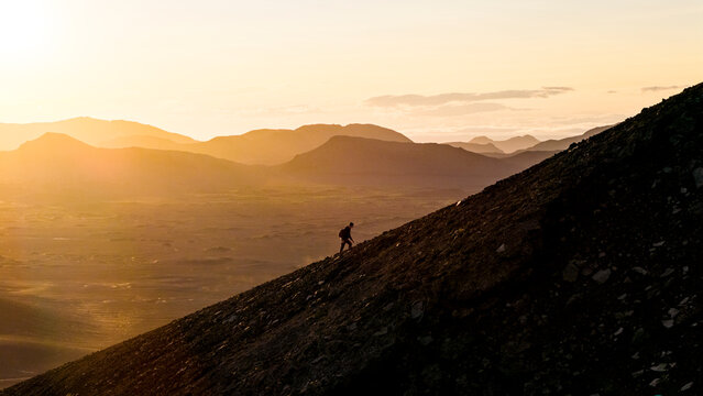 Aerial drone view of a silhouette person walking uphill on Blahylur Crater during sunset in the highlands of Iceland.