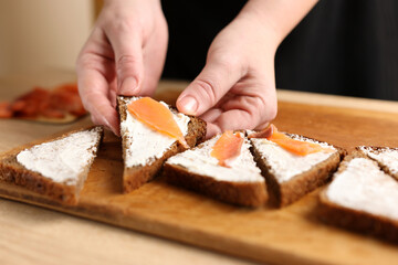 A piece of salmon is added to black bread with cheese. Preparation of canapes with fish