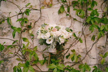 Wedding bouquet hangs in the branches of green ivy on an old stone building