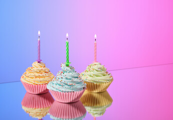Birthday sweet decoration. Cupcakes with colored whipped cream and sprinkles. Colored burning candles. Copy space for text.