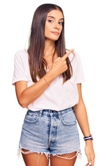 Fototapeta premium Young hispanic woman wearing casual white tshirt pointing with hand finger to the side showing advertisement, serious and calm face