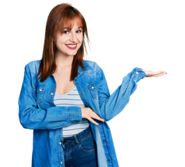 Redhead young woman wearing casual denim jacket smiling cheerful presenting and pointing with palm of hand looking at the camera.