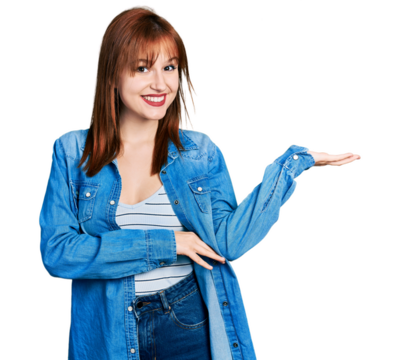 Redhead young woman wearing casual denim jacket smiling cheerful presenting and pointing with palm of hand looking at the camera.