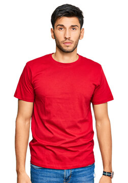Young handsome man wearing casual red tshirt relaxed with serious expression on face. simple and natural looking at the camera.