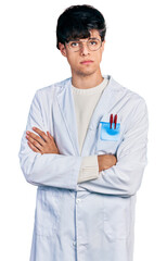 Handsome hipster young man with crossed arms wearing doctor uniform relaxed with serious expression on face. simple and natural looking at the camera.