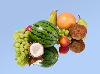Fruit and berry composition on the mirror. Ripe watermelon, sweet grapes, coconut, pears and others.