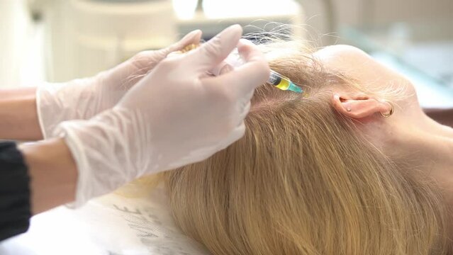 Cosmetologist makes a blond woman prp therapy against hair loss, injections in the scalp in a beauty salon. PRP for hair. The concept of cosmetology.