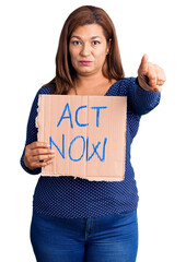 Fototapeta na wymiar Middle age latin woman holding act now banner pointing with finger to the camera and to you, confident gesture looking serious