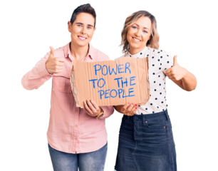 Couple of women holding power to the people banner smiling happy and positive, thumb up doing excellent and approval sign