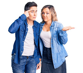 Couple of women wearing casual clothes confused and annoyed with open palm showing copy space and pointing finger to forehead. think about it.