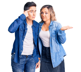 Couple of women wearing casual clothes confused and annoyed with open palm showing copy space and pointing finger to forehead. think about it.