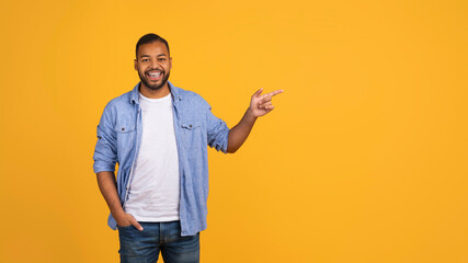 Joyful young black man pointing aside at copy space on yellow background