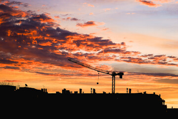 Sunset behind silhouette of cityscape with construction crane.