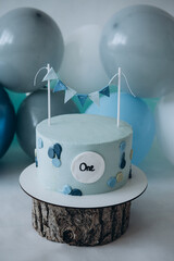 Blue cake on a wooden stand  with decorative flags. The first cake. Cake on a white background. Blue and white balloons. Birthday. First birthday. Holiday
