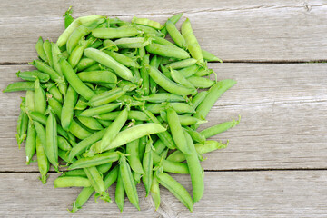 A pile of fresh green pea pods on a wooden background with a place for text.Cultivation, care, harvesting, harvesting peas for winter, breeding, agronomy, vegetarianism, protein production.