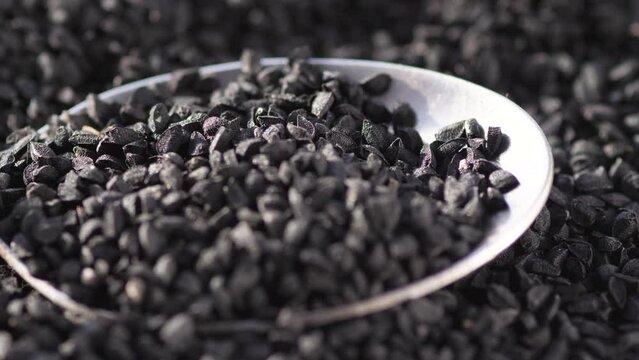 macro black cumin seeds heap in a spoon rotation. black cumin seeds benefits in cooking and medicine