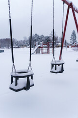 Swings covered in snow at the empty playground in winter.