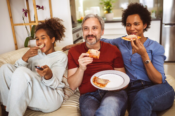 Portrait of happy family sharing pizza at home and watching tv.