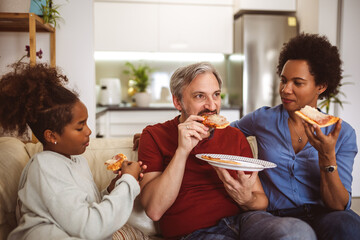 Portrait of happy family sharing pizza at home and watching tv. - obrazy, fototapety, plakaty