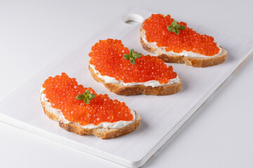 Three sandwiches with red caviar on a cutting board. A delicious appetizer of trout caviar on a slice of bread with cream cheese. Salted salmon caviar for fish delicacy concept