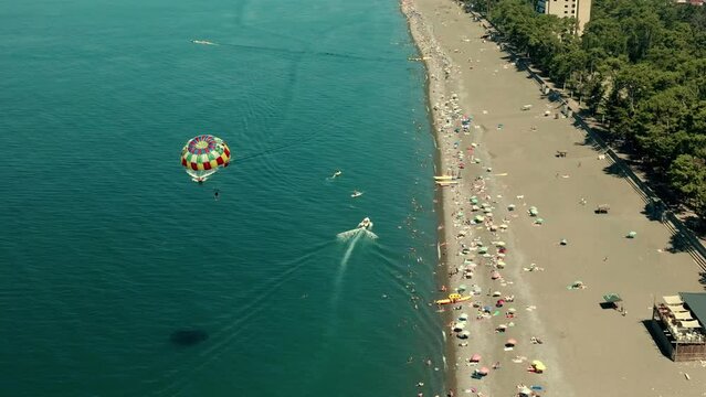Parasailing in blue sea drone view. Aerial view parasailing in sea bay. Colorful parasail wing pulled by sailing boat in turquoise ocean water. 