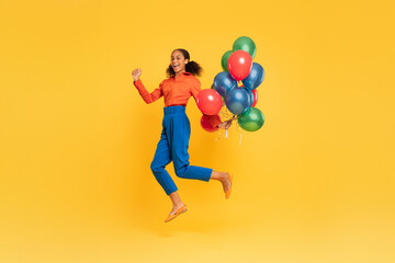 Fototapeta na wymiar Cheerful black teen girl jumping with bunch of balloons, studio