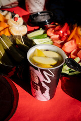 Vivid picnic close-up with artistically designed coffee cup, fresh sliced apples, and colorful veggies on red fabric