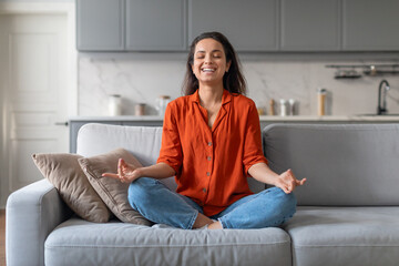 Obraz premium Serene woman practicing mindfulness meditation on a cozy sofa at home