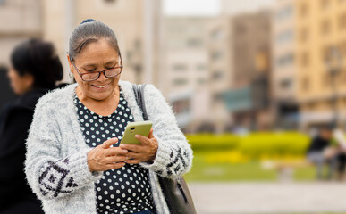 Latina adult woman, with a happy expression, in the city using her smartphone, sending audio messages and typing. Copyspace......