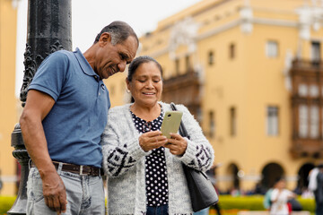 Multiracial adult couple happily using their mobile phones while strolling through the city on a beautiful day. Copyspace