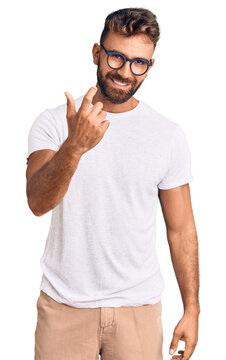 Young hispanic man wearing casual clothes and glasses beckoning come here gesture with hand inviting welcoming happy and smiling
