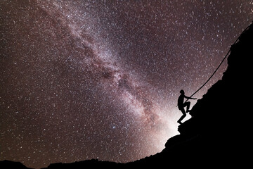 Silhouette of climber climbing  on the rock, on the milky way galaxy background.