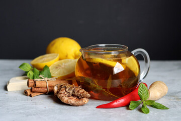 Teapot with hot tea, ginger, turmeric root, cinnamon sticks, lemon and mint leaves on grey background with copy space. Anti inflammatory winter drink recipe. 