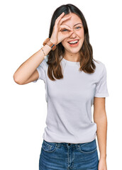 Fototapeta premium Young beautiful woman wearing casual white t shirt doing ok gesture with hand smiling, eye looking through fingers with happy face.