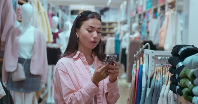 Amidst clothing racks woman's joy while texting in mobile phone and shopping reflects modern tech-savvy shopping. Joy selecting fashionable items symbol wealth Shopping joy mix style technology.