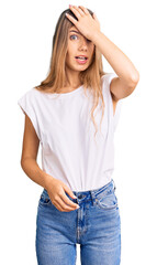 Beautiful caucasian woman with blonde hair wearing casual white tshirt surprised with hand on head for mistake, remember error. forgot, bad memory concept.